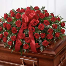 Large red rose casket spray with a red ribbon on a wooden casket