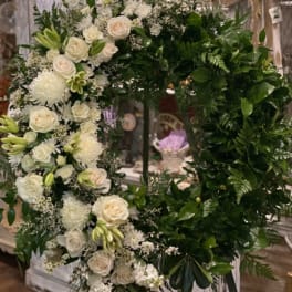 Large white floral wreath on a stand with roses and greenery