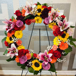 Colorful floral wreath on a black stand with roses, lilies, sunflowers, and daisies