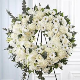 White funeral wreath with roses, lilies, and daisies on a stand