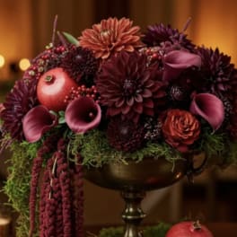 Deep burgundy floral arrangement with calla lilies and pomegranates in a pedestal bowl