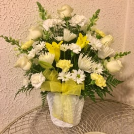White and yellow floral arrangement in a white vase with a yellow ribbon