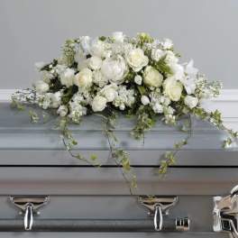 Low white rose and lily arrangement with trailing vines displayed on a silver casket