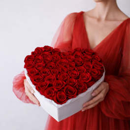 Heart-shaped box of red roses held by a woman in a red dress