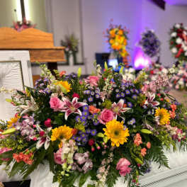 Large mixed floral casket spray with pink, yellow, purple, and white blooms
