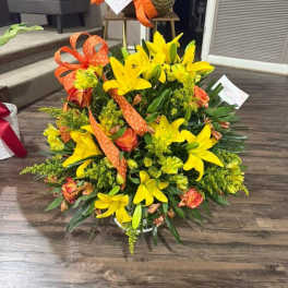 Yellow lilies and orange roses in a low bouquet with orange ribbon