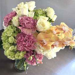 Bouquet of pink carnations, white roses, green hydrangeas, and orange orchids in a glass vase