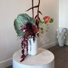 Tall tropical floral arrangement in a white vase with burgundy and green accents