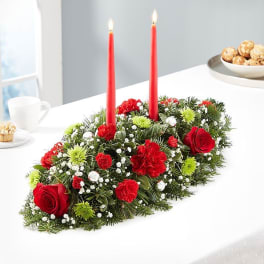 Holiday centerpiece with red candles and red flowers on evergreen