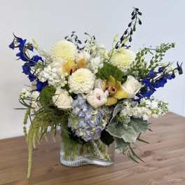 Mixed bouquet in a clear glass vase with blue, white, and yellow flowers