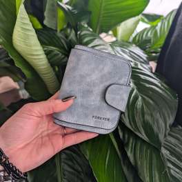 Hand holding a gray wallet in front of large green plant leaves.