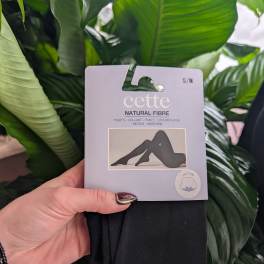 Hand holding packaged black tights in front of large green leaves