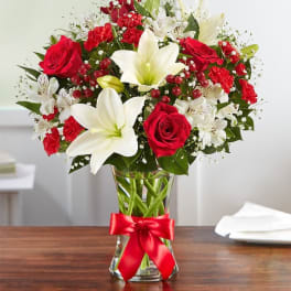 Red roses and white lilies in a glass vase with a red ribbon