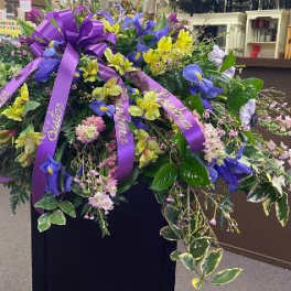 Large purple and yellow floral spray with ribbon on a stand