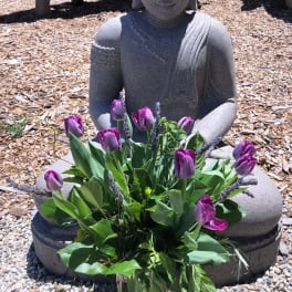 Purple tulips arranged in a glass vase in front of a stone statue