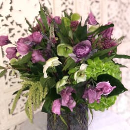 Purple and green mixed bouquet in a dark glass vase