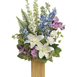 Tall floral arrangement with white lilies, blue and pink flowers in a wooden vase