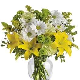 Yellow lilies with white daisies and green flowers arranged in a clear glass vase