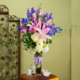 Tall bouquet of pink lilies, roses, and blue irises in a glass vase