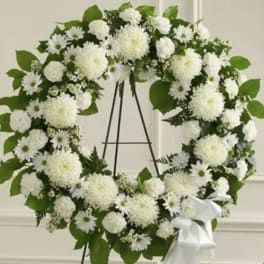 White floral wreath on a black easel with a white ribbon