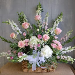 Fan-shaped basket arrangement of pink roses and white flowers with a white bow