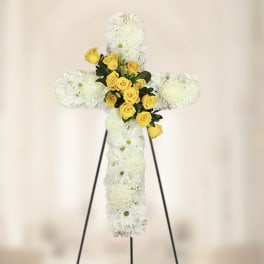 White floral cross with yellow roses on a stand