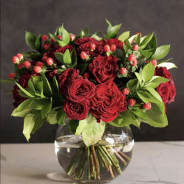 Red rose bouquet in a clear glass vase with green foliage and berry accents