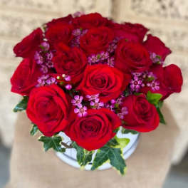 Bouquet of red roses with small purple filler flowers in a white vase