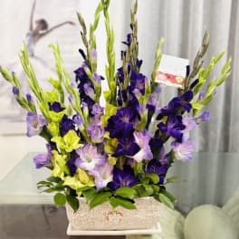 Tall arrangement of purple and yellow gladiolus in a decorative rectangular container