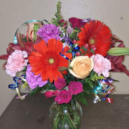 Colorful bouquet of gerbera daisies, roses, and carnations in a glass vase