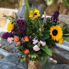 Bouquet with sunflowers, purple lilacs, and pink roses in a burlap-wrapped vase