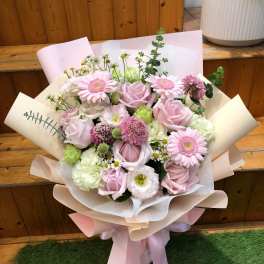 Bouquet of pink roses, gerbera daisies, and mixed blooms wrapped in pastel paper