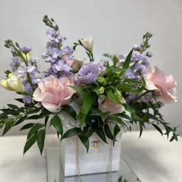 Pink and lavender flowers arranged in a white gift box with a gold chain
