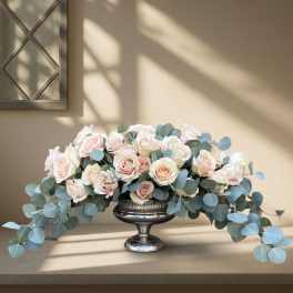 Blush roses arranged in a silver pedestal bowl with trailing eucalyptus