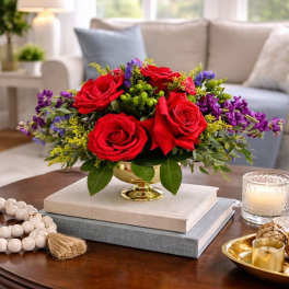 Red roses in a gold vase with purple filler flowers
