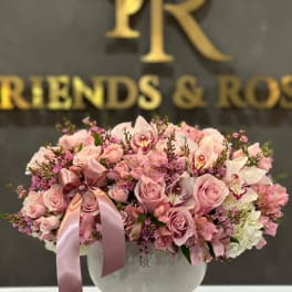 Pink roses and orchids arranged in a white vase with a satin ribbon