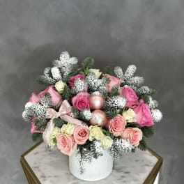 Pink and cream roses arranged in a white vase with frosted evergreen accents.