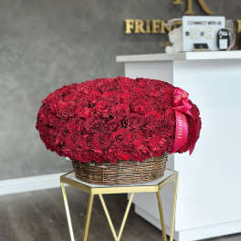 Large red rose arrangement in a wicker basket with a pink ribbon