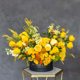Yellow roses and white flowers arranged in a black hat box