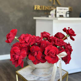 Red roses arranged in a white pedestal vase with a ribbon