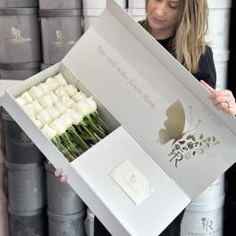 White roses arranged in a presentation box held by a woman