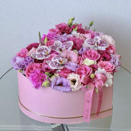 Pink and lavender floral arrangement in a round pink box with ribbon