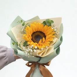Sunflower bouquet wrapped in pale green and cream paper with a brown ribbon
