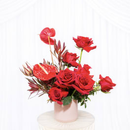 Red roses and anthuriums arranged in a pink vase