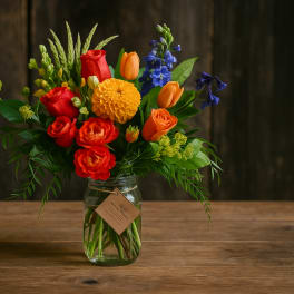 Mixed bouquet of red, orange, yellow, and blue flowers in a glass jar