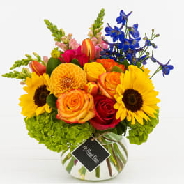 Bright mixed bouquet in a round glass vase with sunflowers and roses