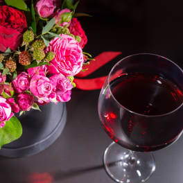 Pink and red rose bouquet beside a glass of red wine