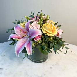 Pink lily and roses in a glass vase with greenery