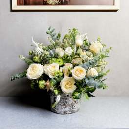 Cream roses in a rustic metal container with mixed greenery
