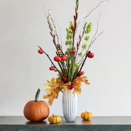 Tall autumn arrangement in a white vase with pumpkins and fall leaves